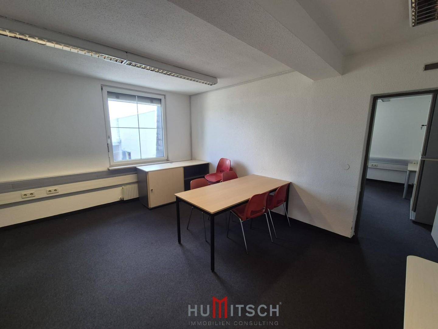 Kleineres Büro mit Teppichboden, einem Tisch und roten Stühlen, ideal für Besprechungen.