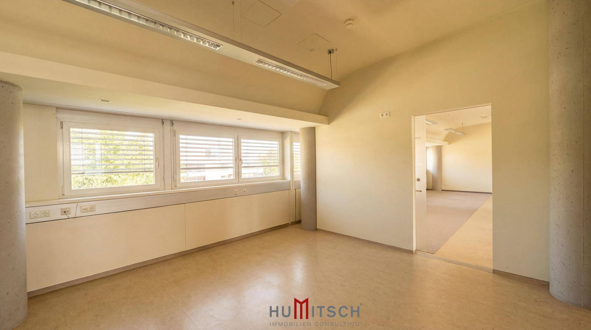 Leeres, helles Büro mit großen Fenstern, die viel Tageslicht hereinlassen und einen weiten Blick bieten.