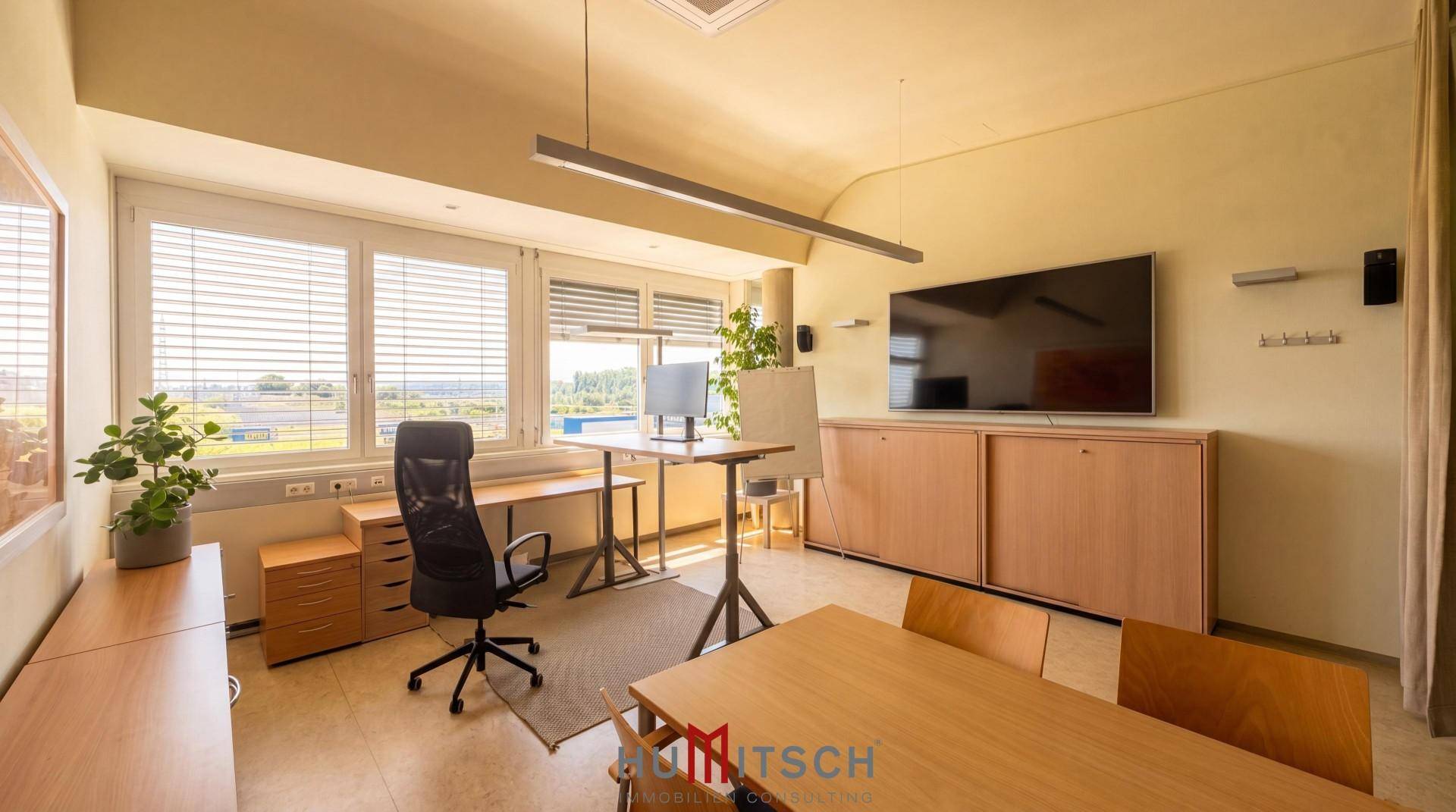 Funktionales Büro mit Schreibtisch, Bürostuhl, großem Fernseher und natürlichem Lichteinfall.