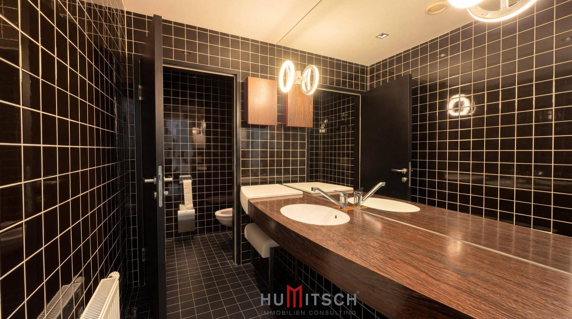 Stilvolles Badezimmer mit schwarzen Fliesen, Doppelwaschbecken und einem großen Spiegel.