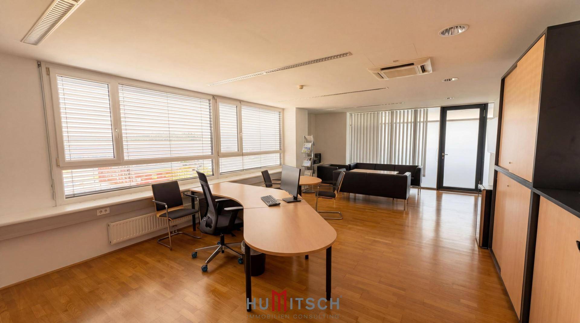 Offener Bürobereich mit mehreren Arbeitsplätzen, Holzparkett und großen Fenstern.