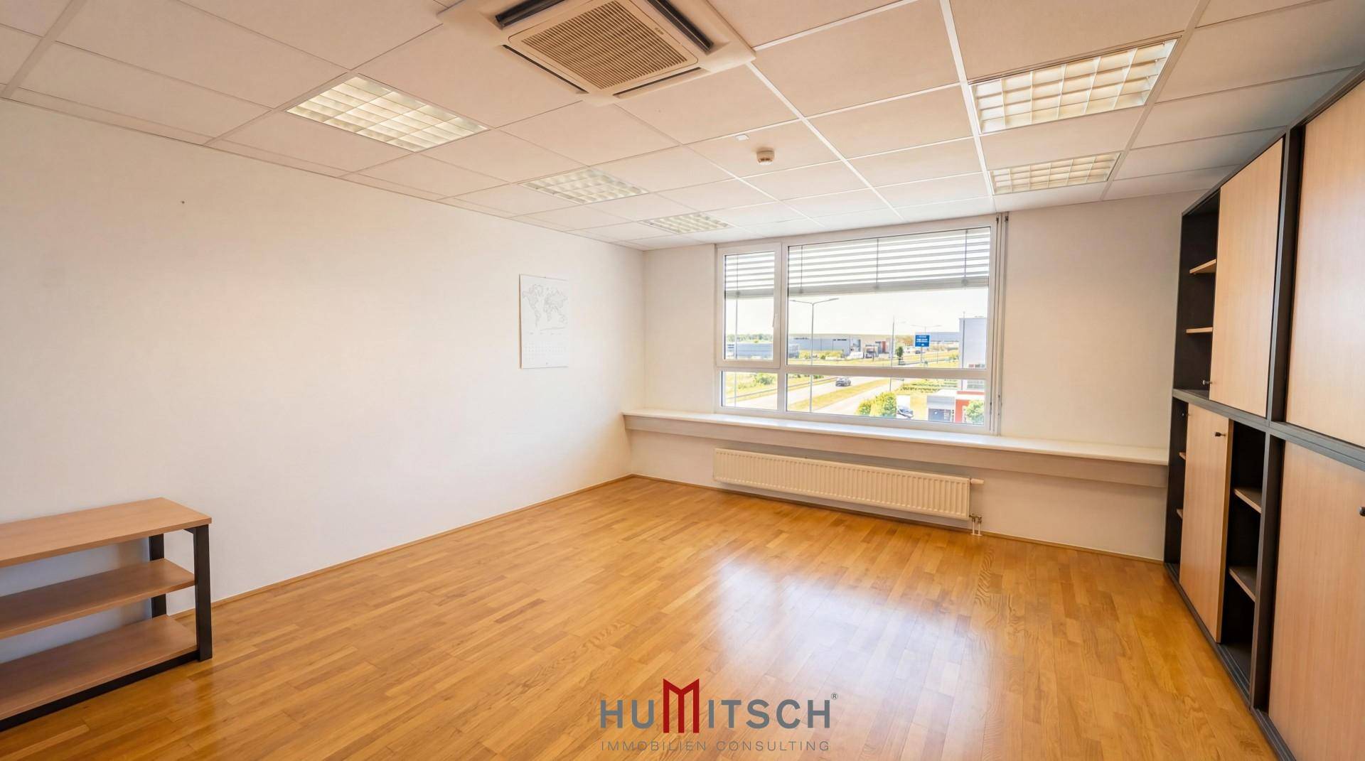 Helles Büro mit Holzparkett, großen Fenstern und Blick auf die Umgebung.