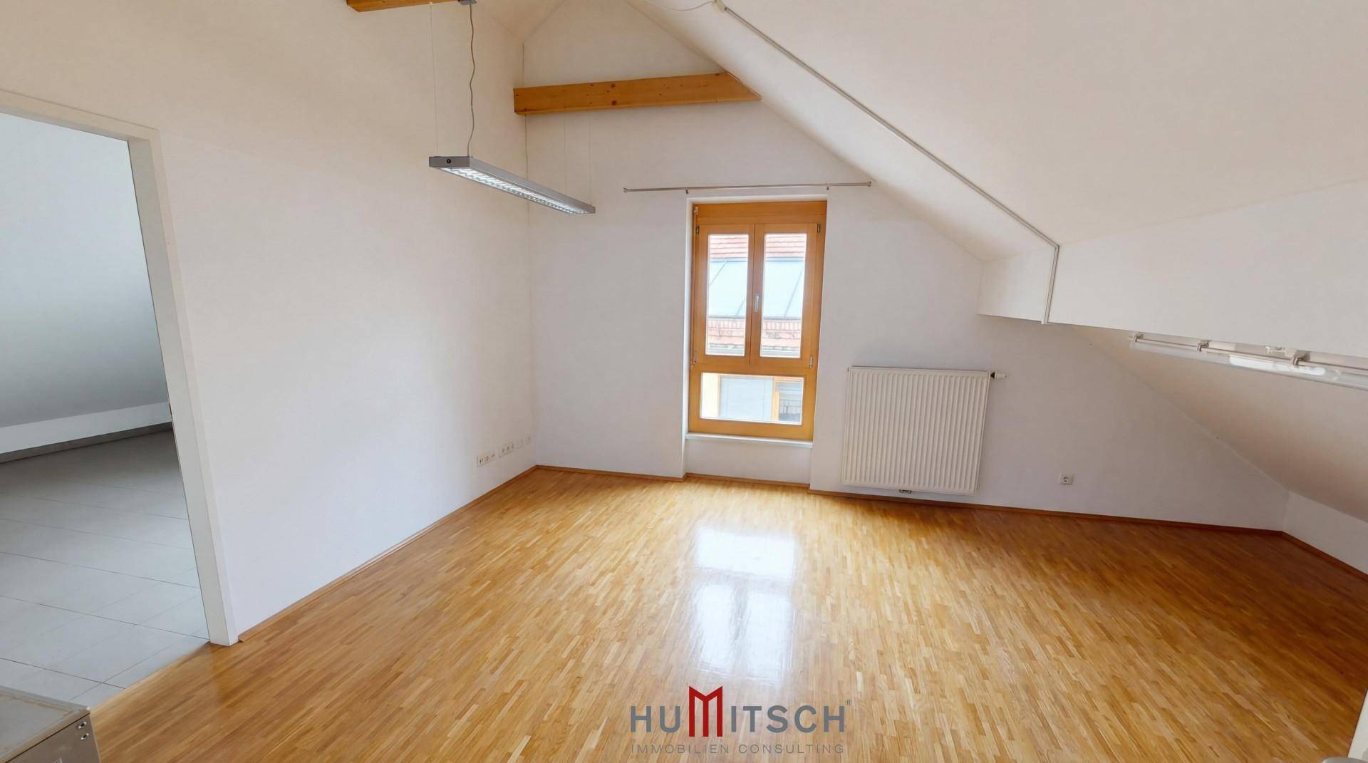 Heller Dachbodenraum mit Holzboden, schrägen Wänden und einem Fenster, das viel Tageslicht hereinlässt.