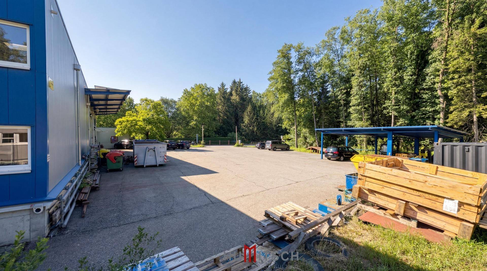 Rückseite des Gewerbegebäudes mit überdachtem Bereich, Lagerflächen und angrenzendem Wald.