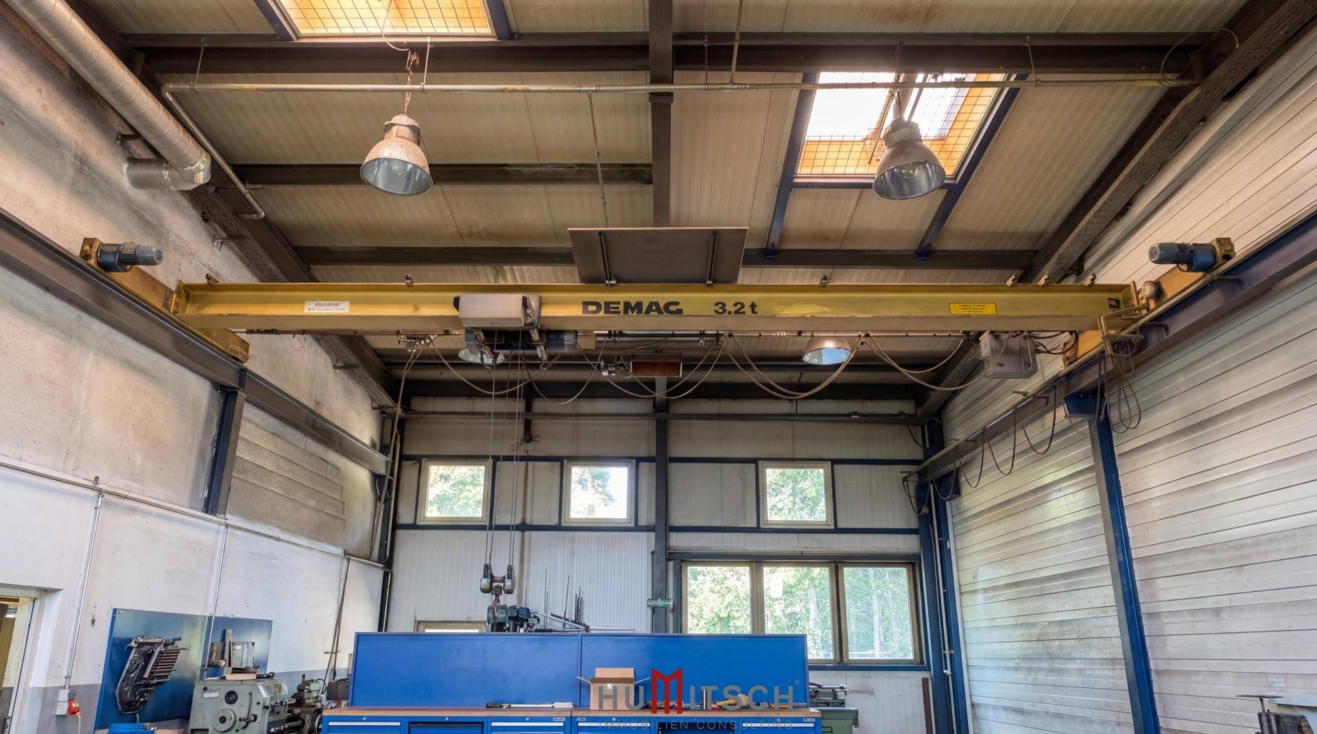 Industrieller Deckenkran (DEMAG 3.2t) in einer Werkstatt mit hohen Fenstern.
