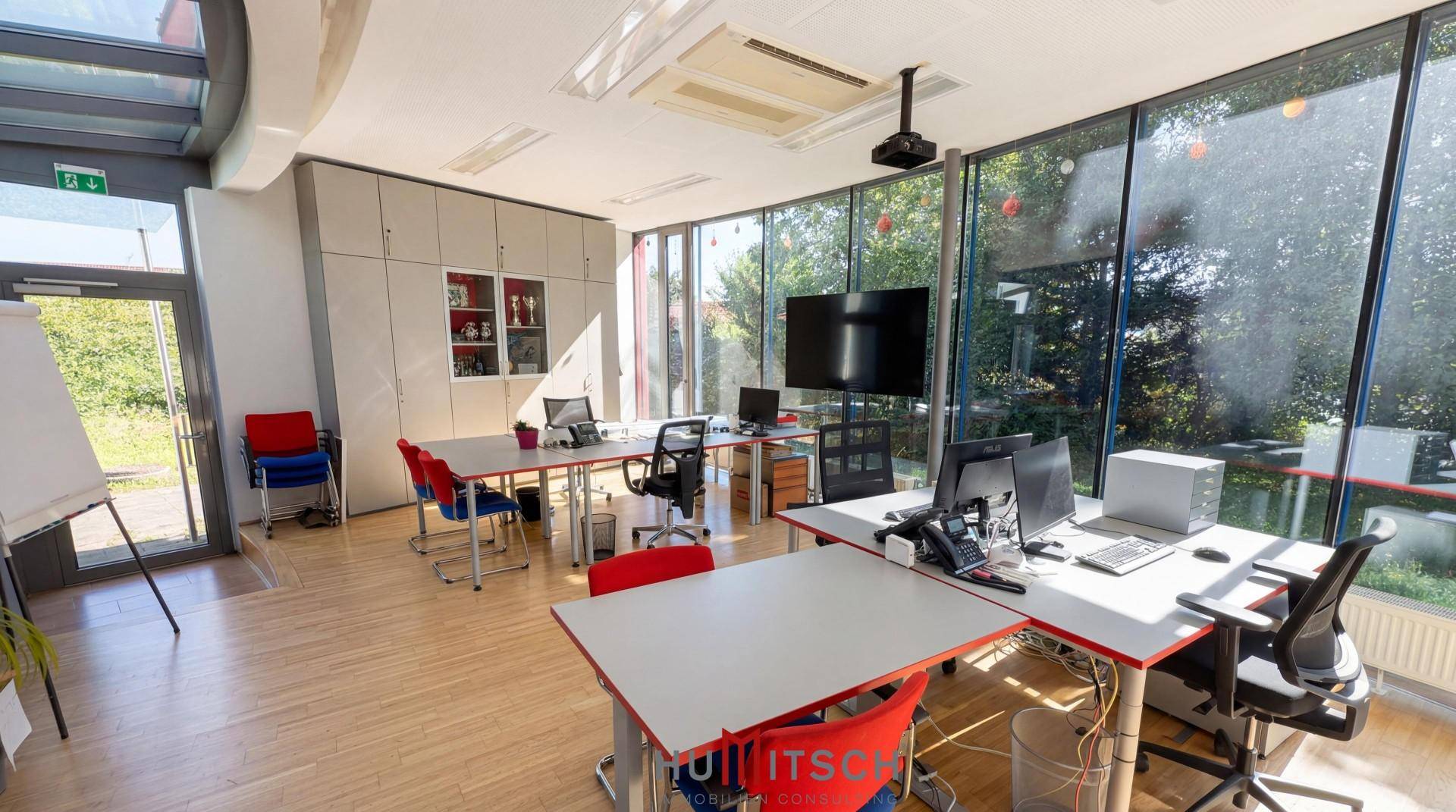Modernes Büro mit großen Glasfronten, Holzboden und mehreren Arbeitsplätzen.