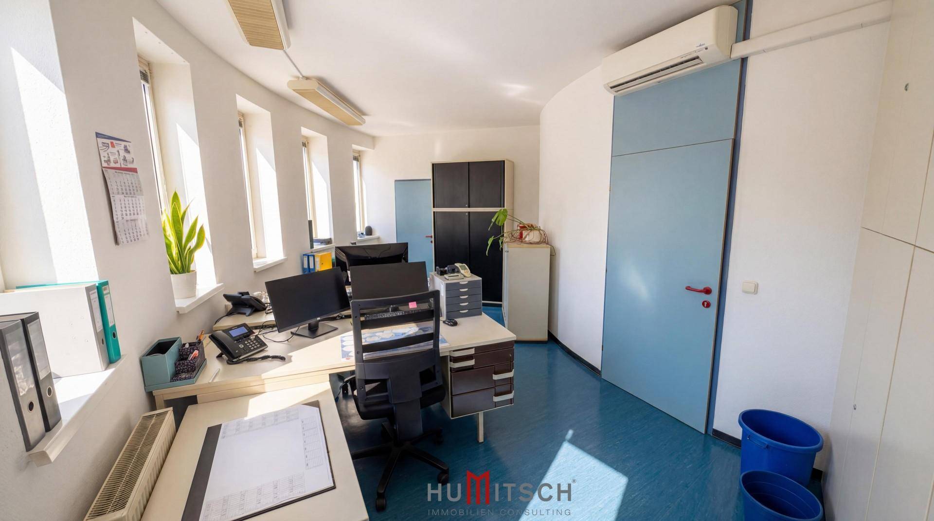 Büro mit mehreren Arbeitsplätzen, Klimaanlage und blauen Akzenten an Türen und Boden.