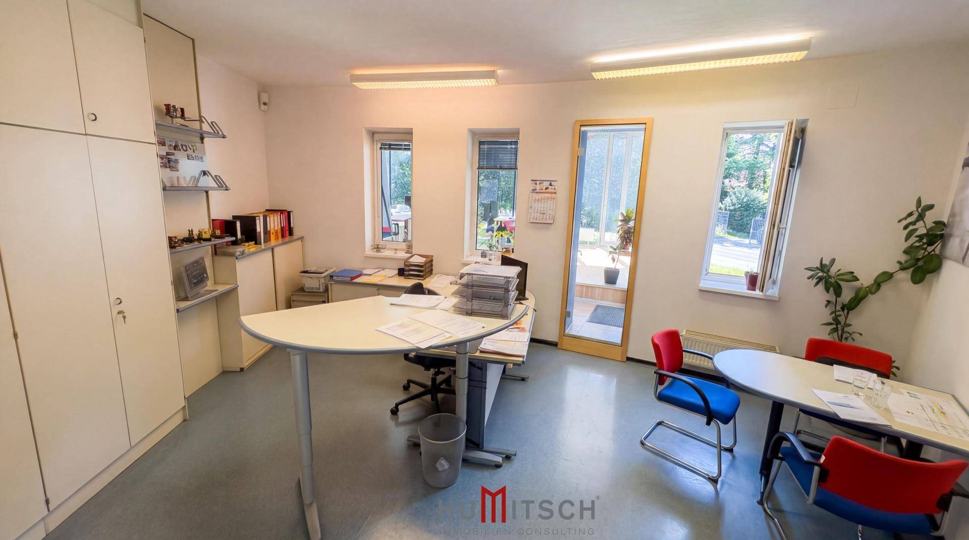 Helles Büro mit mehreren Arbeitsplätzen, Einbauschränken und Fenstern mit Blick ins Grüne.