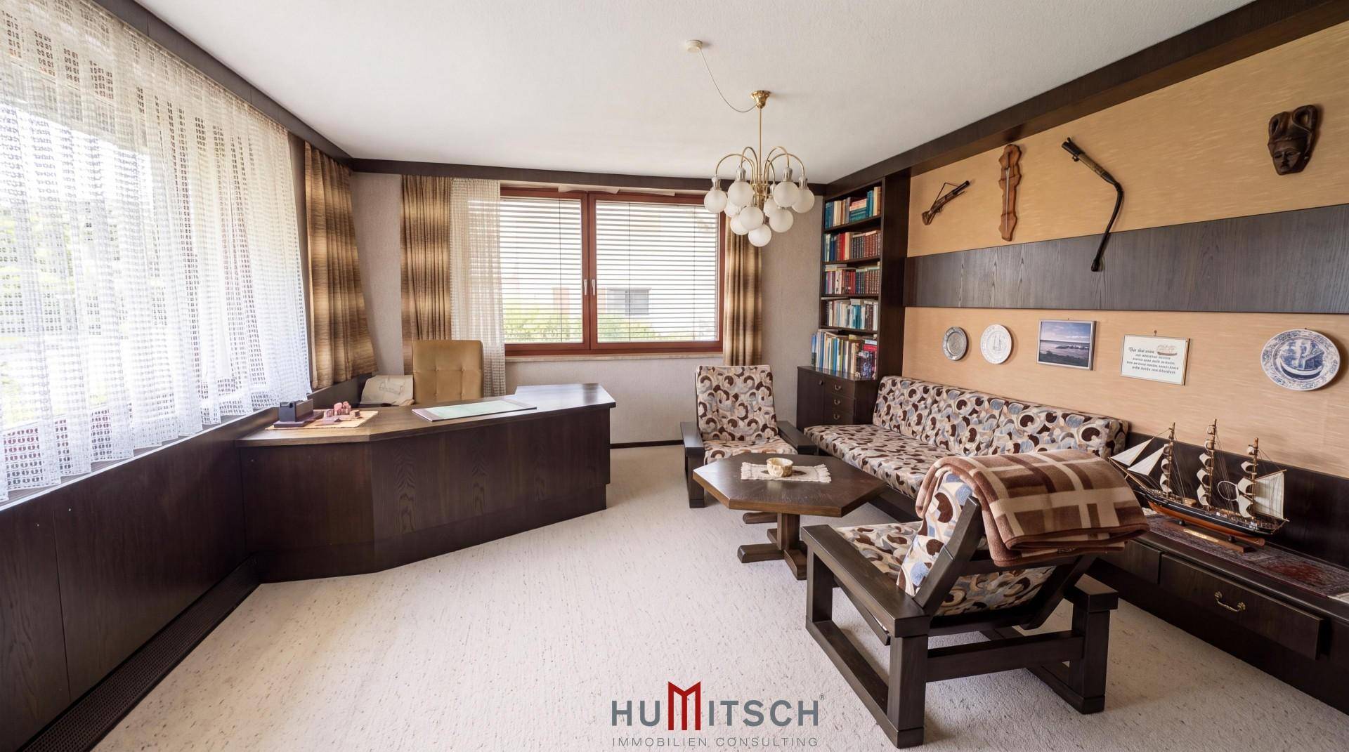Arbeitszimmer mit Schreibtisch, Sofa, Bücherregal und dunkler Holzvertäfelung.