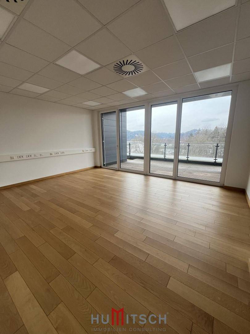Geräumiger Büroraum mit Holzboden und großen Fenstern, die viel Tageslicht hereinlassen.