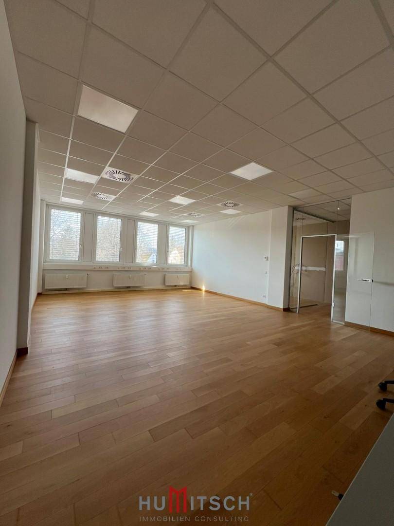 Geräumiger Bürobereich mit Holzboden, großen Fenstern und moderner Glasabtrennung.