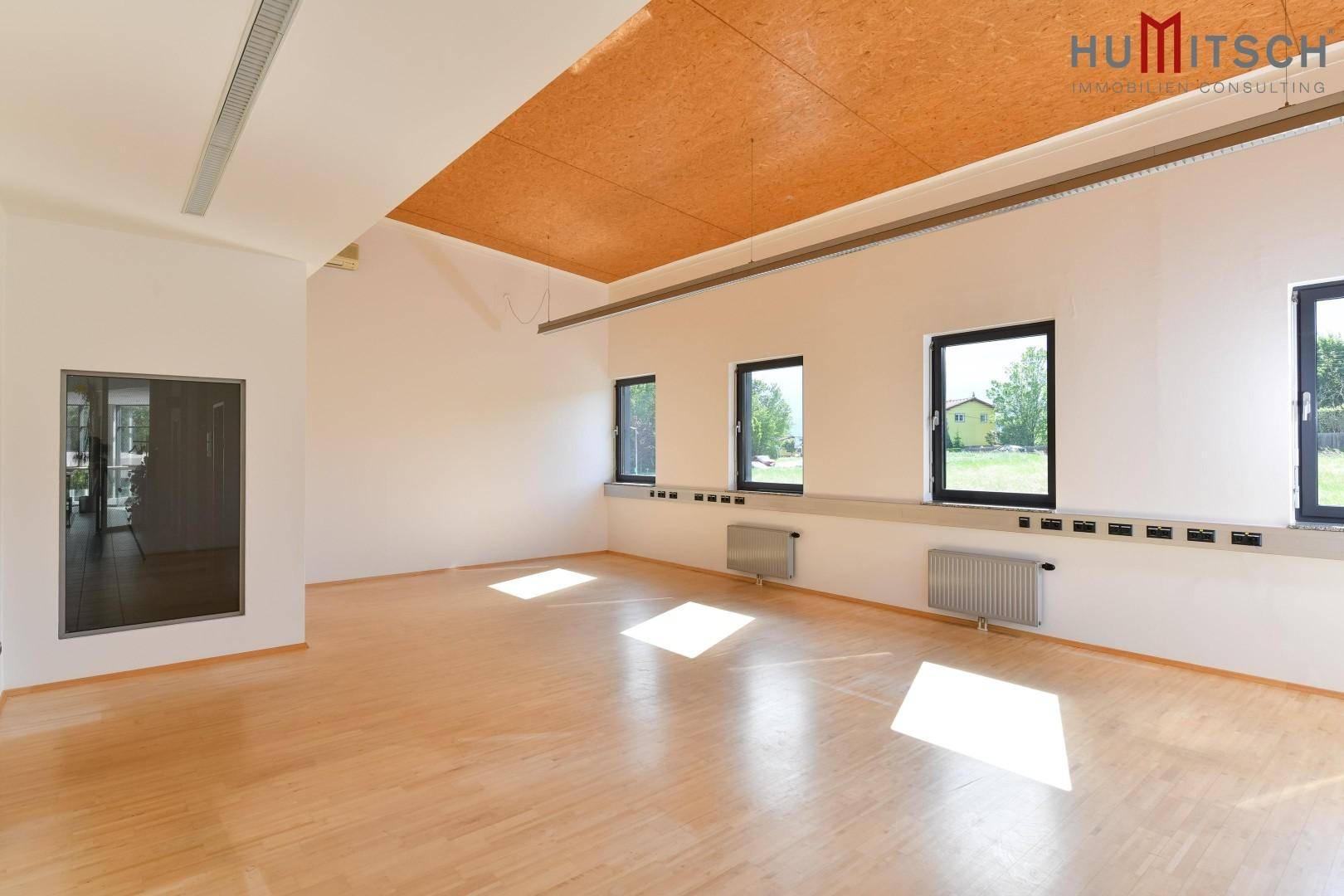 Geräumiges Büro mit Holzboden, mehreren Fenstern und viel Tageslicht, ideal für Arbeitsplätze.