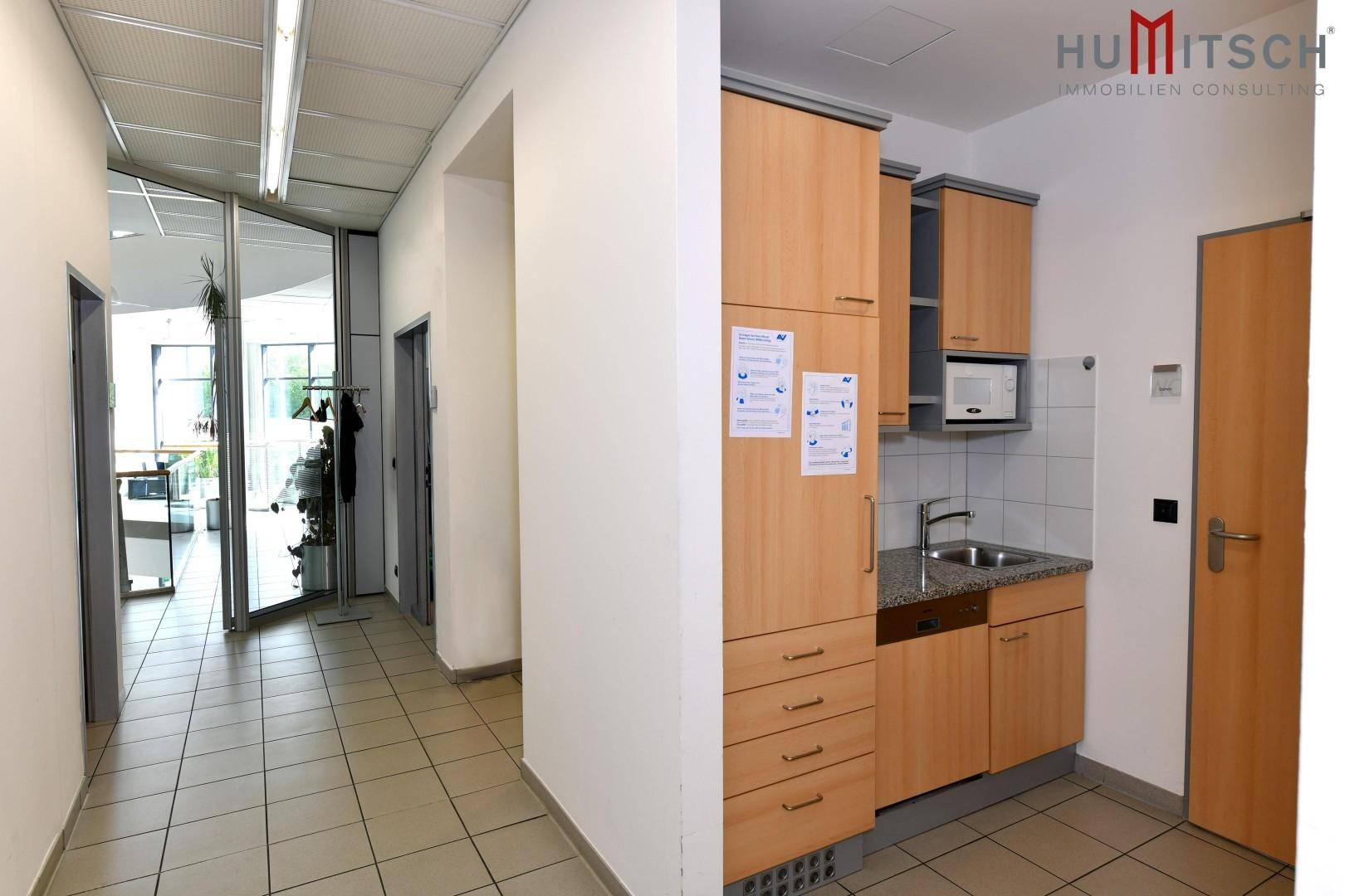Kleiner Küchenbereich in einem Flur mit Holzschränken und Fliesenboden.
