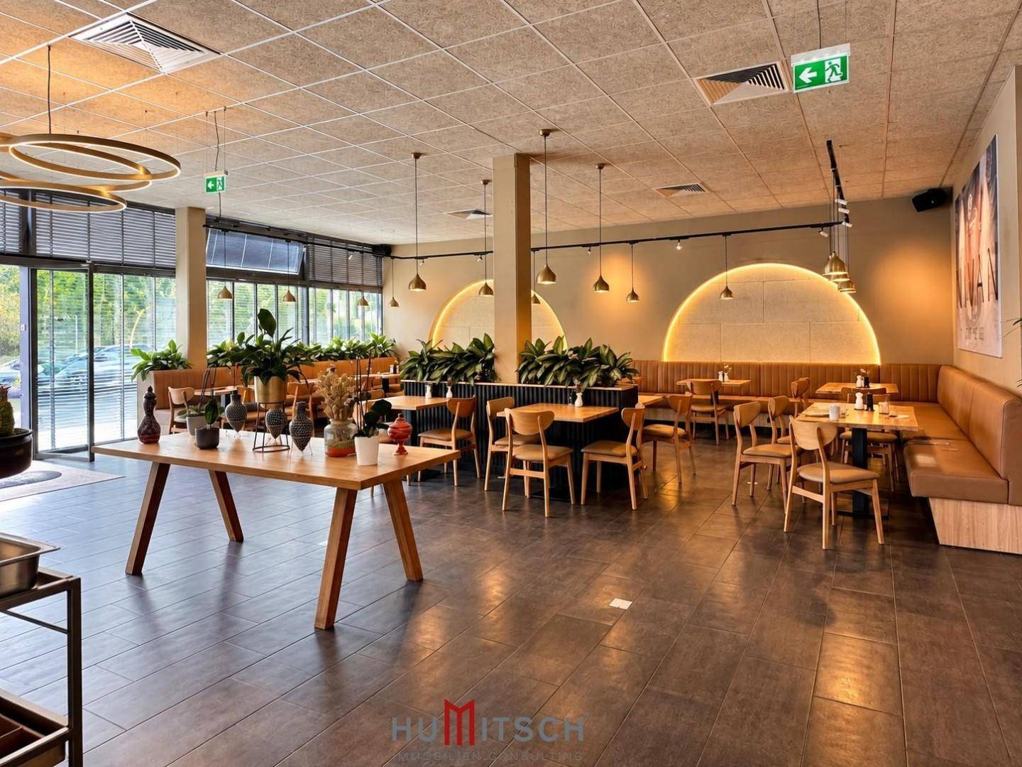 Geräumiger Restaurantbereich mit verschiedenen Sitzbereichen, einem langen Holztisch und indirekter Wandbeleuchtung.