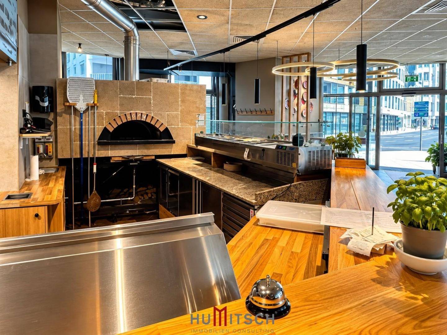 Detailansicht der Gewerbeküche mit gemauertem Pizzaofen, Granitarbeitsplatte und Blick zur Straße.