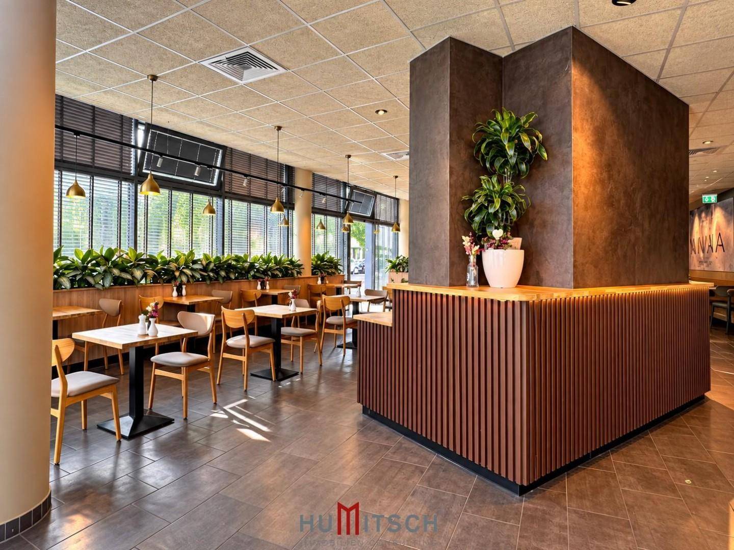 Heller Restaurantbereich mit vielen Sitzgelegenheiten, grünen Pflanzen und einer eleganten Holzverkleidung.