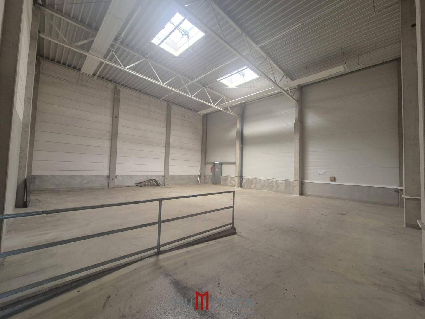 Leere Lagerhalle mit Betonboden, hohen Decken und einer Absperrung im Vordergrund.