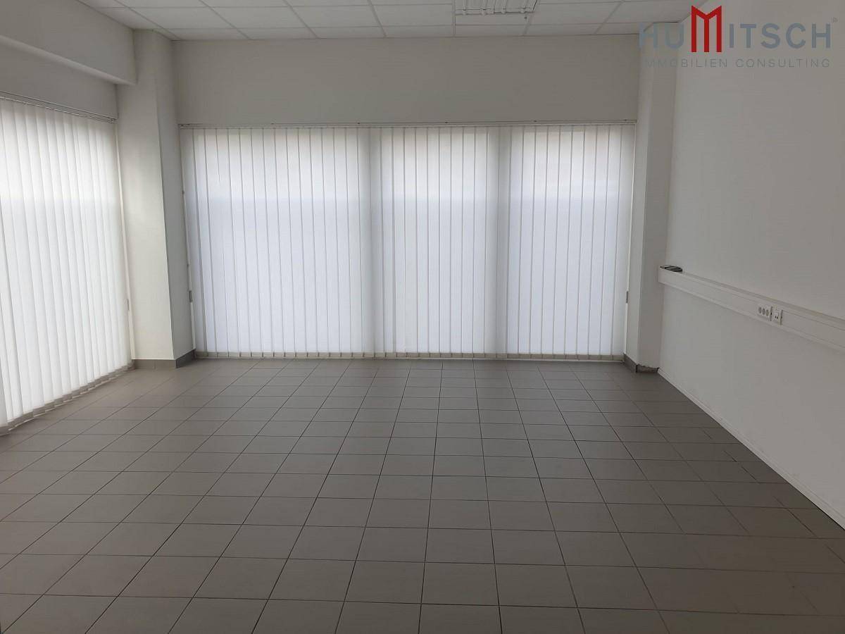 Heller Büroraum mit Fliesenboden und vertikalen Jalousien an den Fenstern für Sichtschutz.