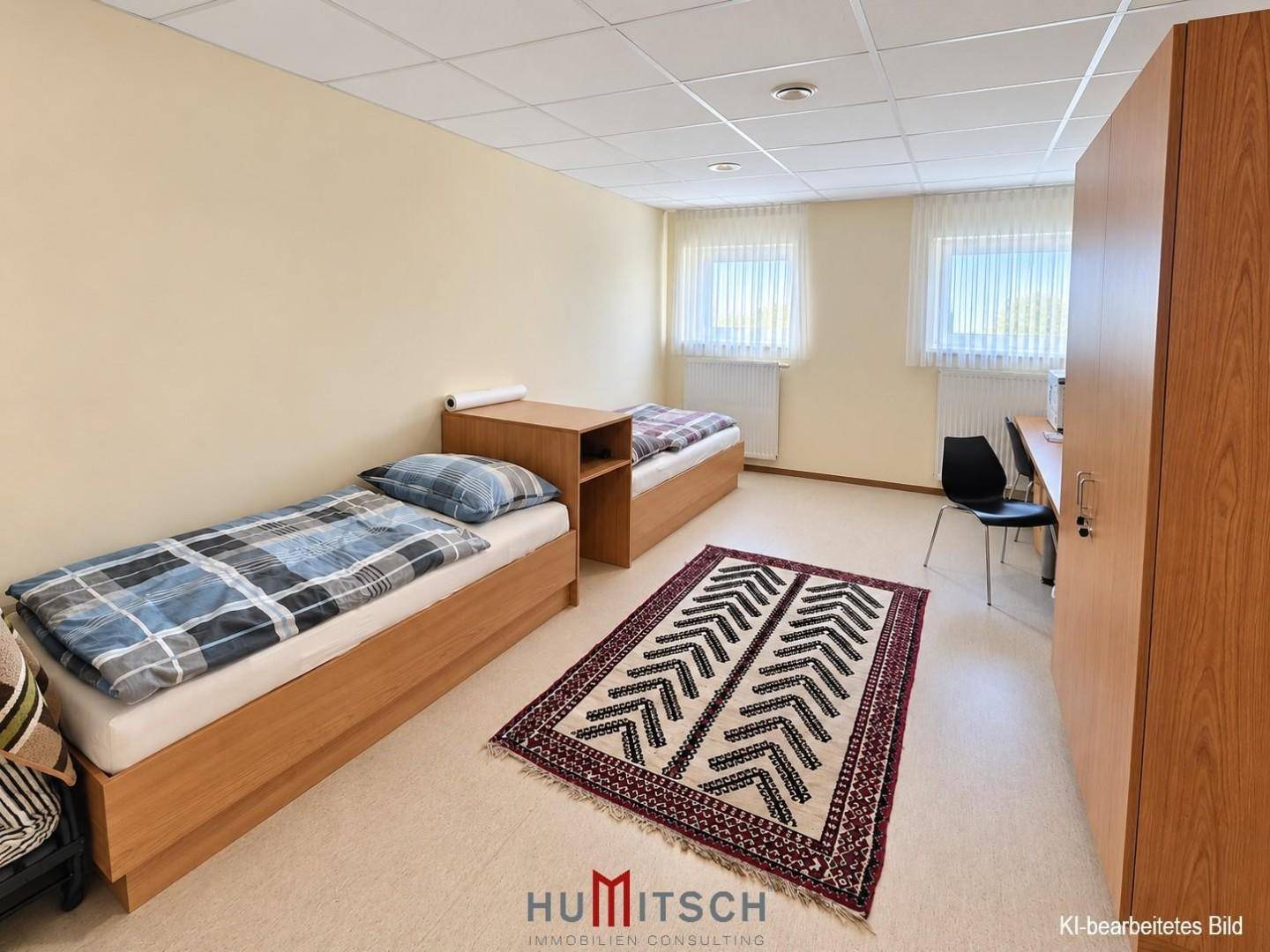 Einfaches Schlafzimmer mit zwei Einzelbetten, Holzmöbeln und hellen Wänden, ideal für Gäste oder Personal.