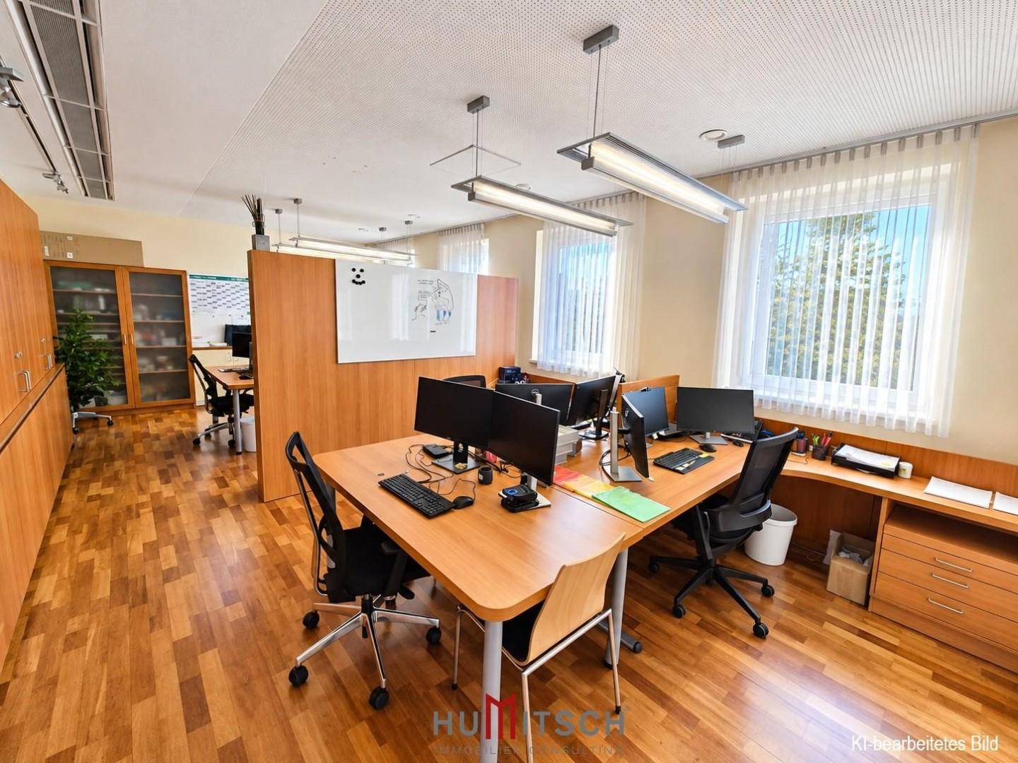 Offener Bürobereich mit mehreren Schreibtischen, Holzmöbeln und großen Fenstern, die viel Licht hereinlassen.