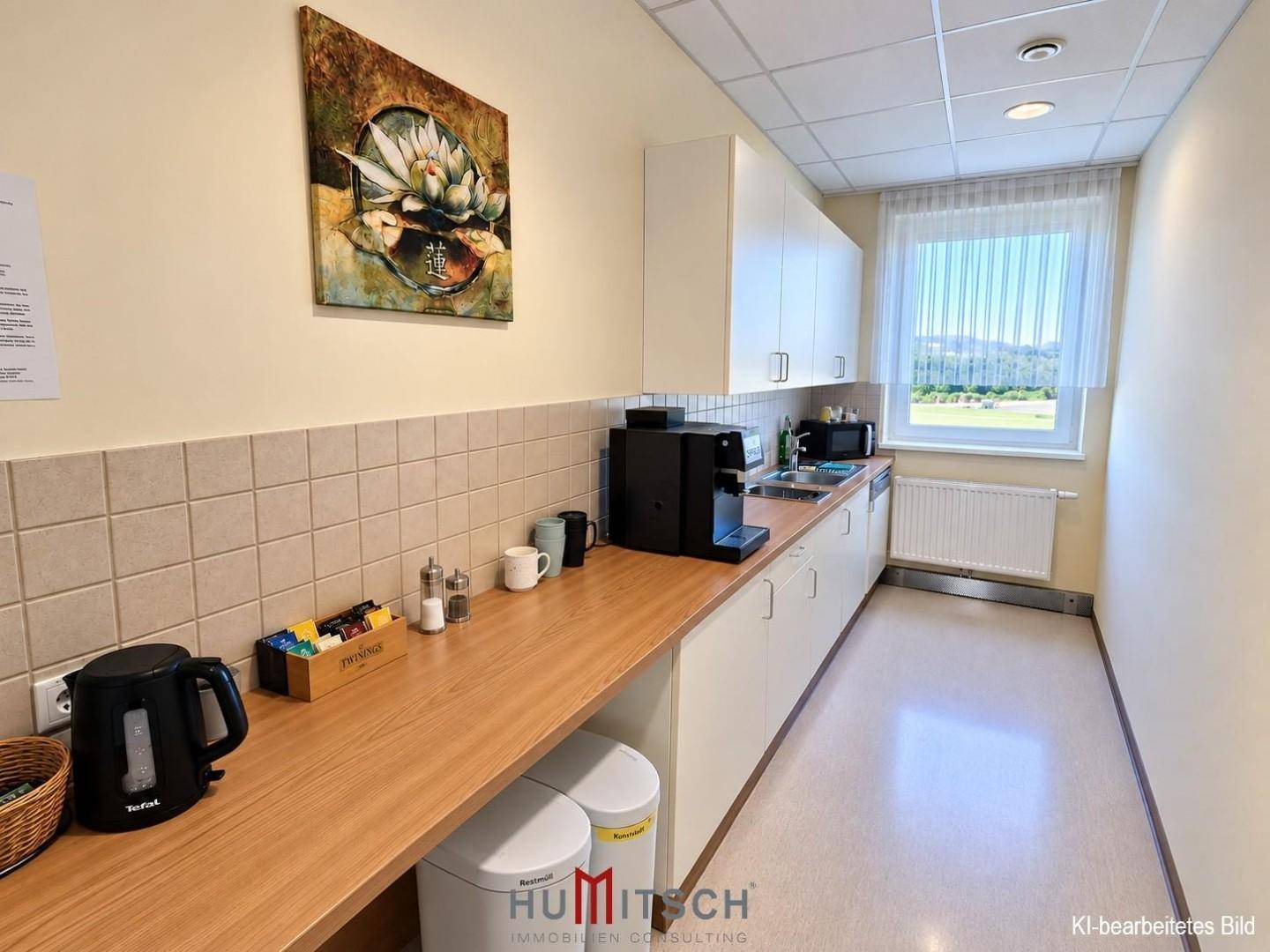 Kleine Teeküche mit Holzarbeitsplatte, Kaffeemaschine und Fenster mit Blick ins Grüne.