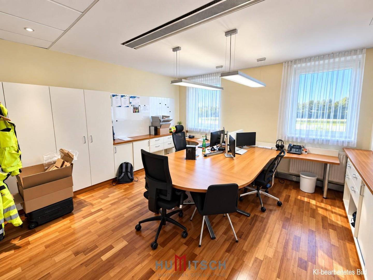 Geräumiges Büro mit Holzboden, mehreren Arbeitsplätzen und weißen Schränken.