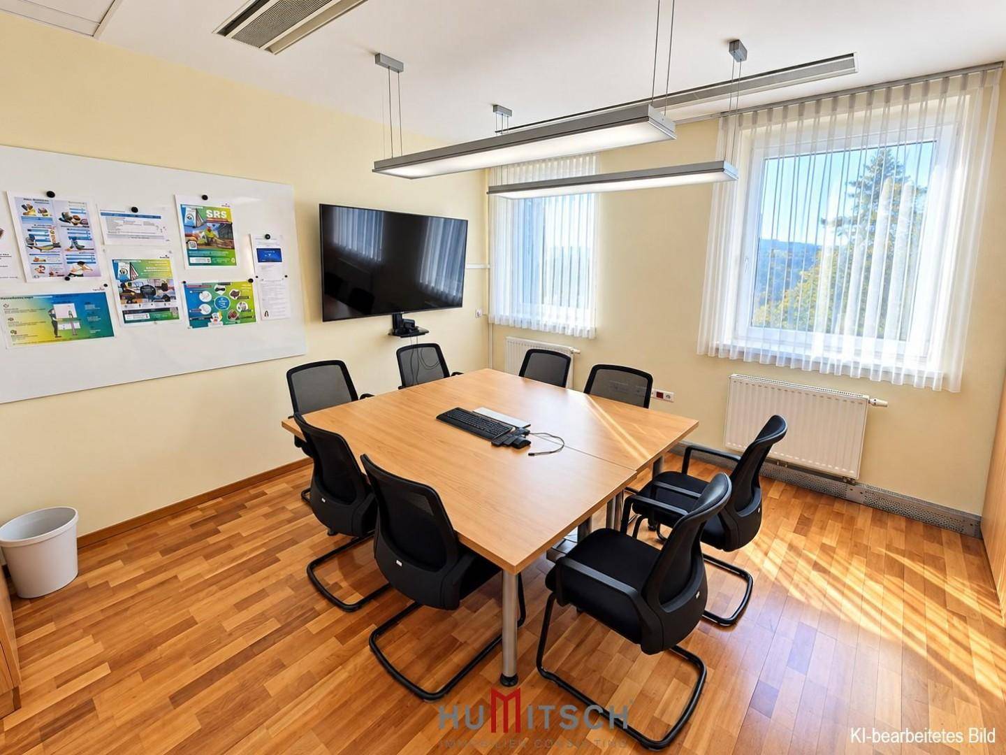 Konferenzraum mit Holzboden, großem Tisch, Stühlen und einem Wandfernseher.