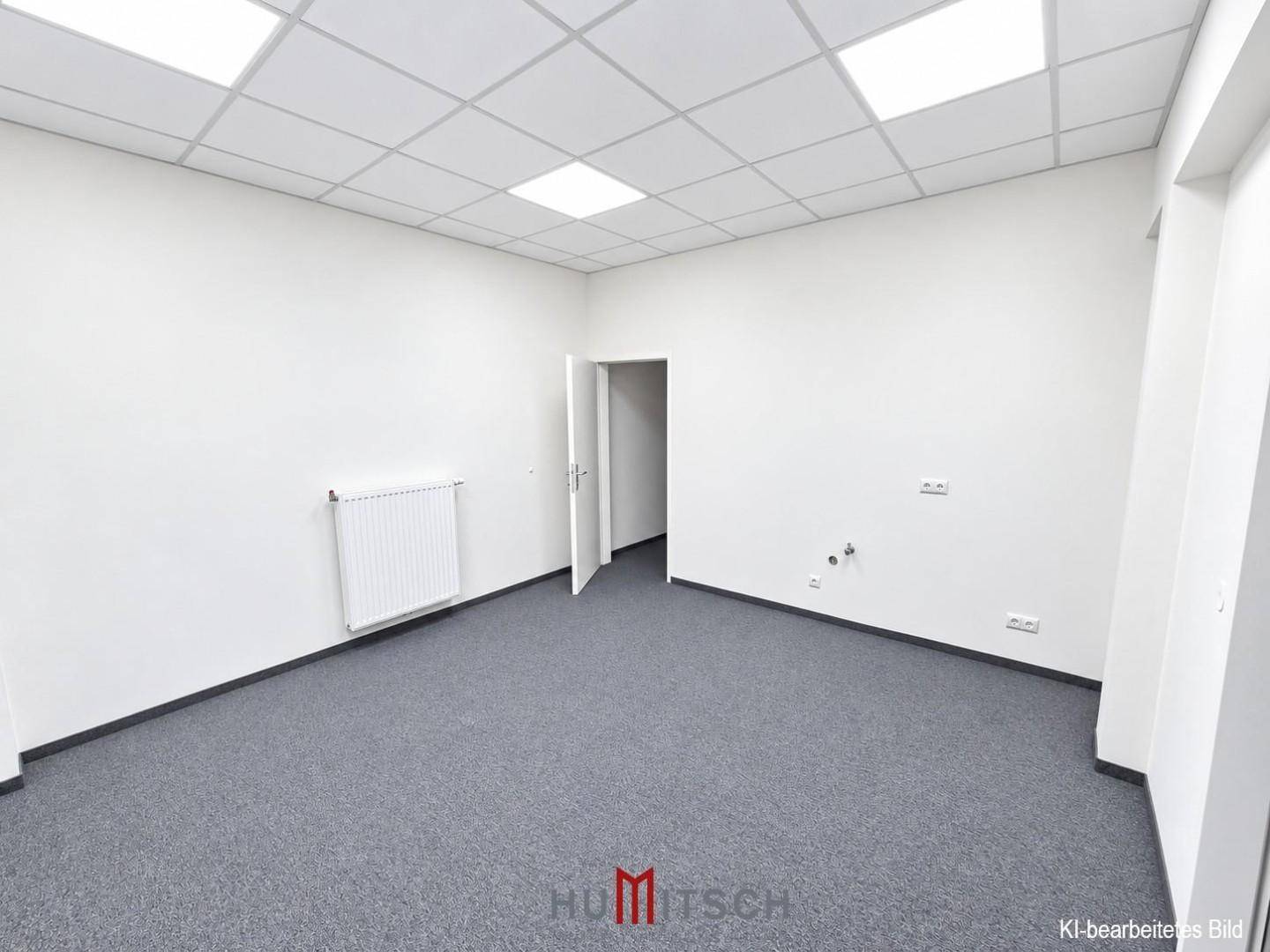 Leerer Büroraum mit Teppichboden, Heizkörper und Anschlüssen an der Wand.