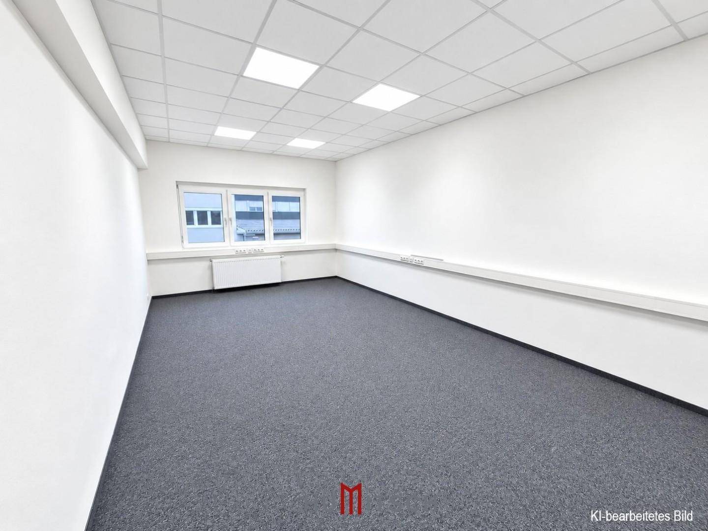 Kleineres, leeres Büro mit Teppichboden, einem Fenster und weiß gestrichenen Wänden.