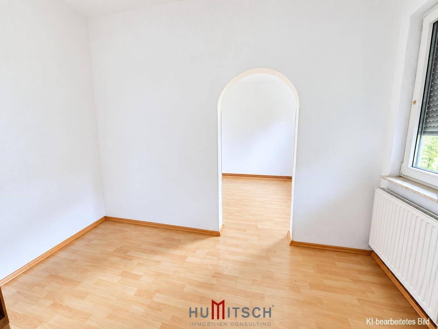 Leerer Raum mit Laminatboden und einem Rundbogen, der zu einem weiteren Zimmer führt.