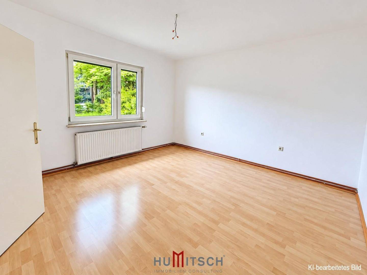 Heller, leerer Raum mit Laminatboden, weiß gestrichenen Wänden und einem großen Fenster.