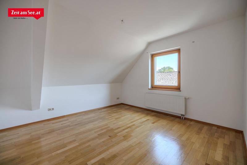 Geräumiges Zimmer im Dachgeschoss mit Holzboden, weiß gestrichenen Wänden und einem Fenster.