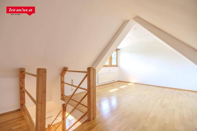 Heller Wohnbereich im Dachgeschoss mit Holztreppe und Holzboden, der zu weiteren Räumen führt.
