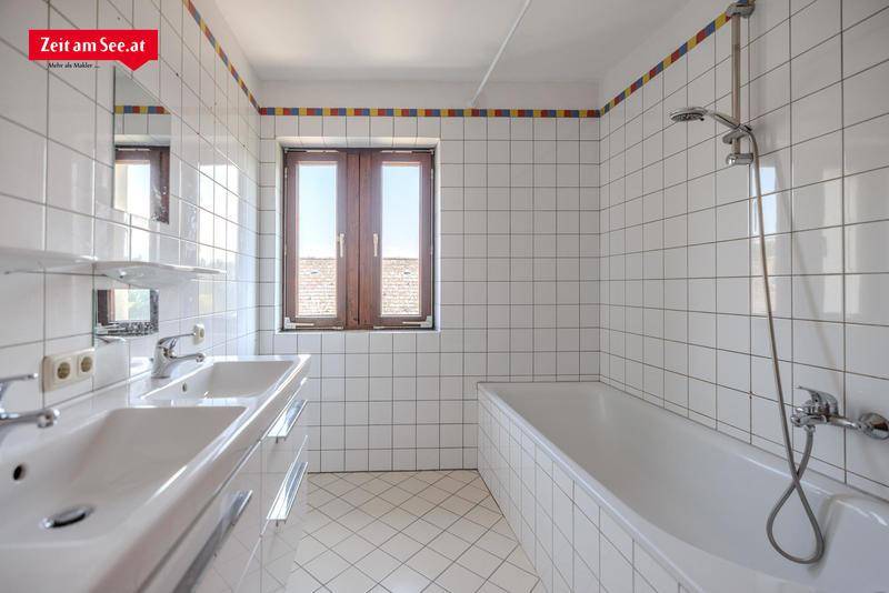 Gefliestes Badezimmer mit Doppelwaschbecken, Badewanne und Fenster, dekoriert mit farbigen Fliesen.