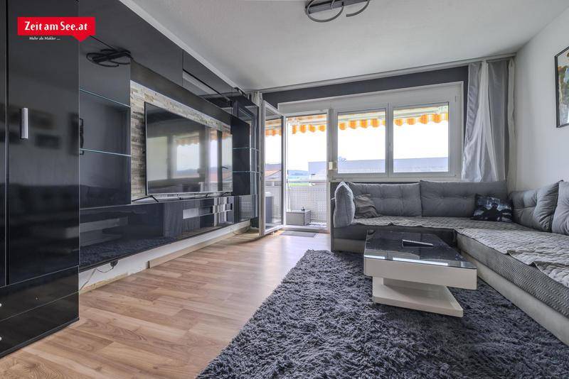 Heller Wohnbereich mit großem Sofa, dunklem TV-Möbel und Zugang zum sonnigen Balkon.
