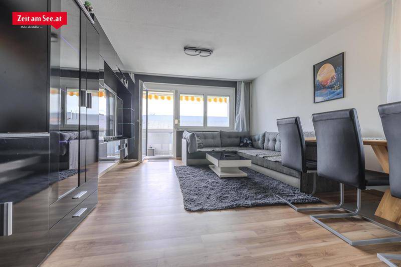 Moderner Wohn-Essbereich mit dunklen Möbeln, Holzboden und Zugang zum Balkon.