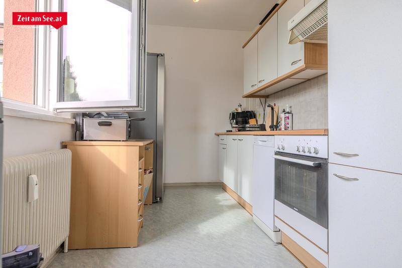 Funktionale Küche mit weißen Schränken, Holz-Arbeitsplatte und Fenster.