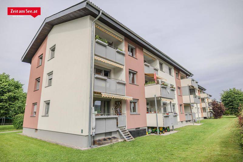 Mehrfamilienhaus mit rosa und weißen Fassaden, Balkonen und grüner Umgebung.