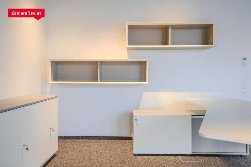 Heller Büroraum mit schwebenden Regalen, weißen Schränken und Teppichboden, ideal für konzentriertes Arbeiten.
