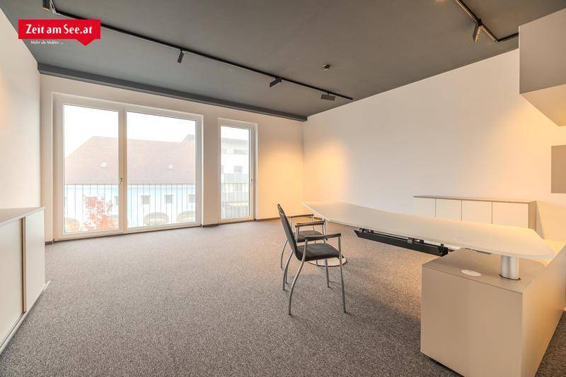 Heller Büroraum mit Teppichboden, großen Fenstern und einem modernen Schreibtisch, der viel Platz bietet.
