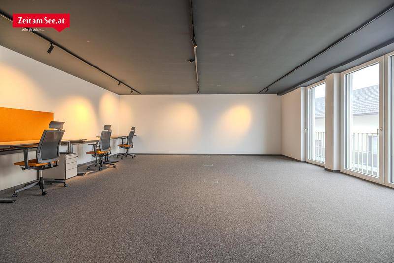 Großer, offener Bürobereich mit Teppichboden, mehreren Arbeitsplätzen und großen Fenstern für viel Licht.