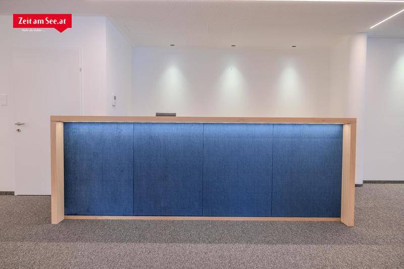 Nahaufnahme eines modernen Empfangstresens mit blauer Stoffverkleidung und hellem Holzrahmen in einem Büro.