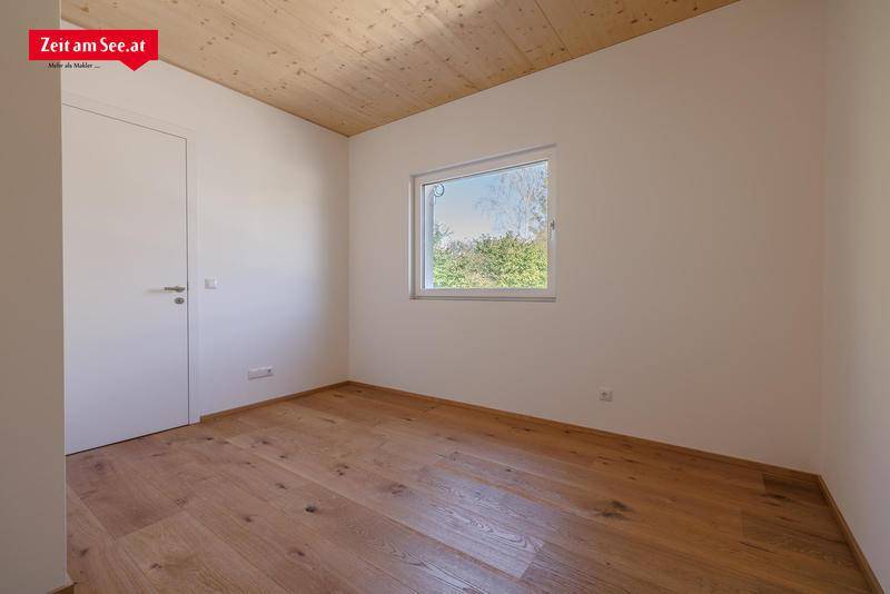 Helles Schlafzimmer mit Holzboden, Holzdecke und einem Fenster mit Blick ins Grüne.
