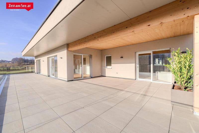 Große, sonnige Terrasse mit Fliesenboden und Zugang zu mehreren Räumen des Neubaus.