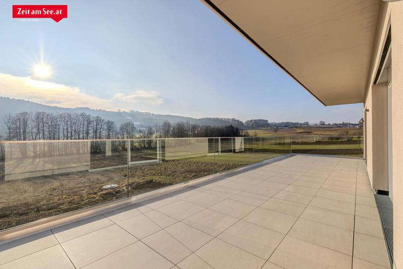 Weitläufige Terrasse mit Glasgeländer und sonnigem Ausblick auf die umliegende Landschaft und Hügel.