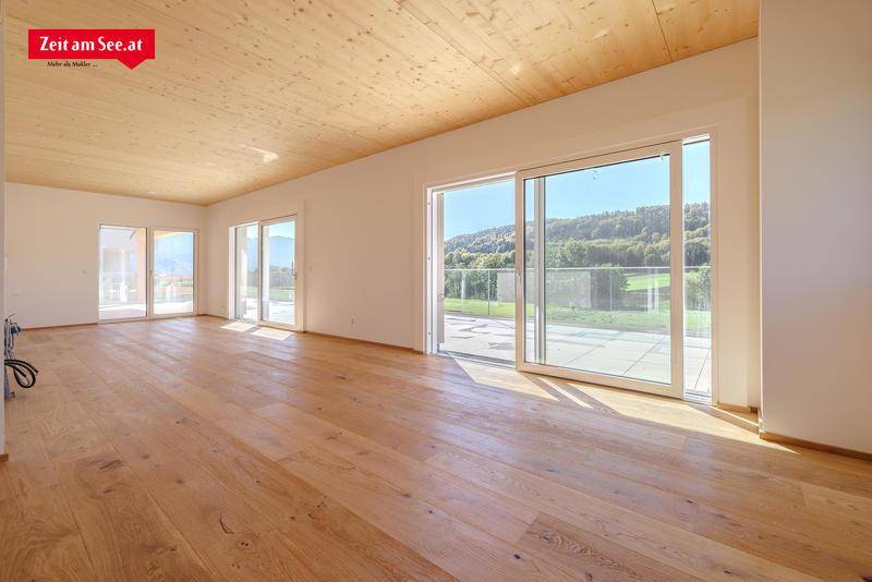 Heller, geräumiger Wohnbereich mit Holzboden, Holzdecke und großen Schiebetüren zur Terrasse.