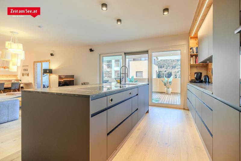 Moderne Küche mit großer Kochinsel, integrierter Spüle und Zugang zur Terrasse mit Bergblick.