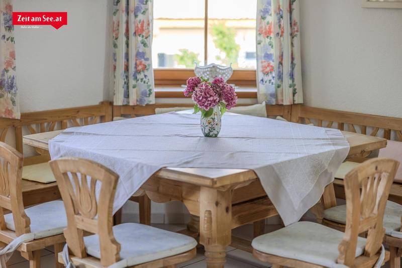 Detailansicht des Esstisches mit traditionellen Holzstühlen und floralen Vorhängen.