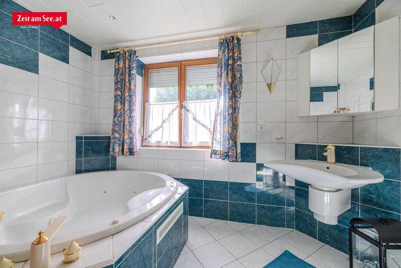 Badezimmer mit blauen und weißen Fliesen, Eckbadewanne und Fenster.