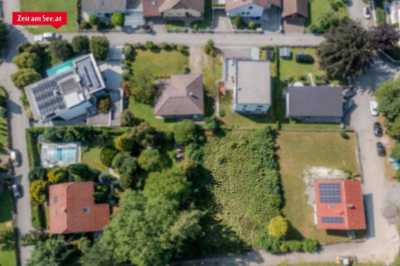 Vogelperspektive eines grünen Grundstücks umgeben von Wohnhäusern, einige mit Solaranlagen und Pool.